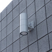 Silver up/down LED cylinder wall light mounted to a block exterior wall in daylight