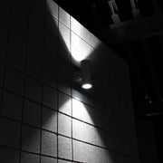 Architectural LED cylinder light casting up and down beams on wall at night