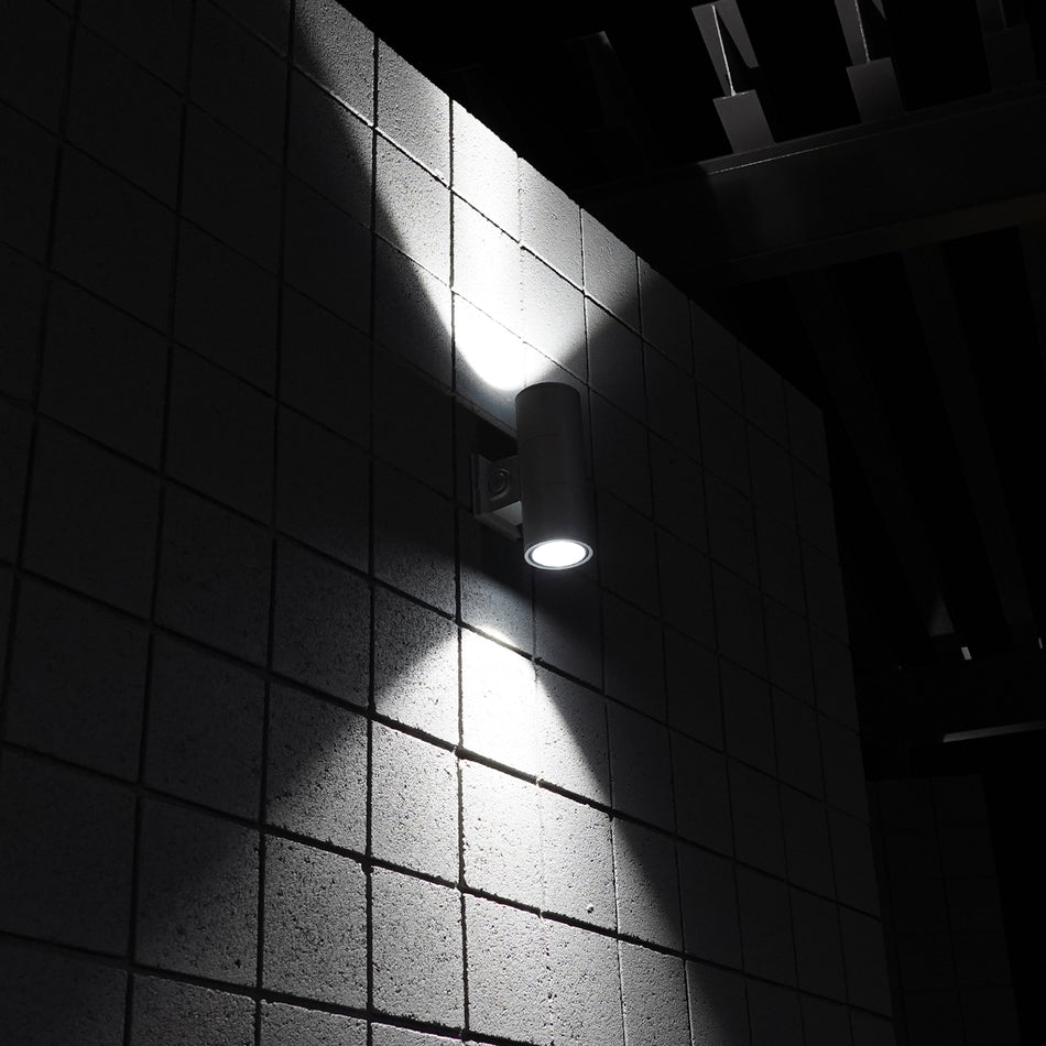 Architectural LED cylinder light casting up and down beams on wall at night